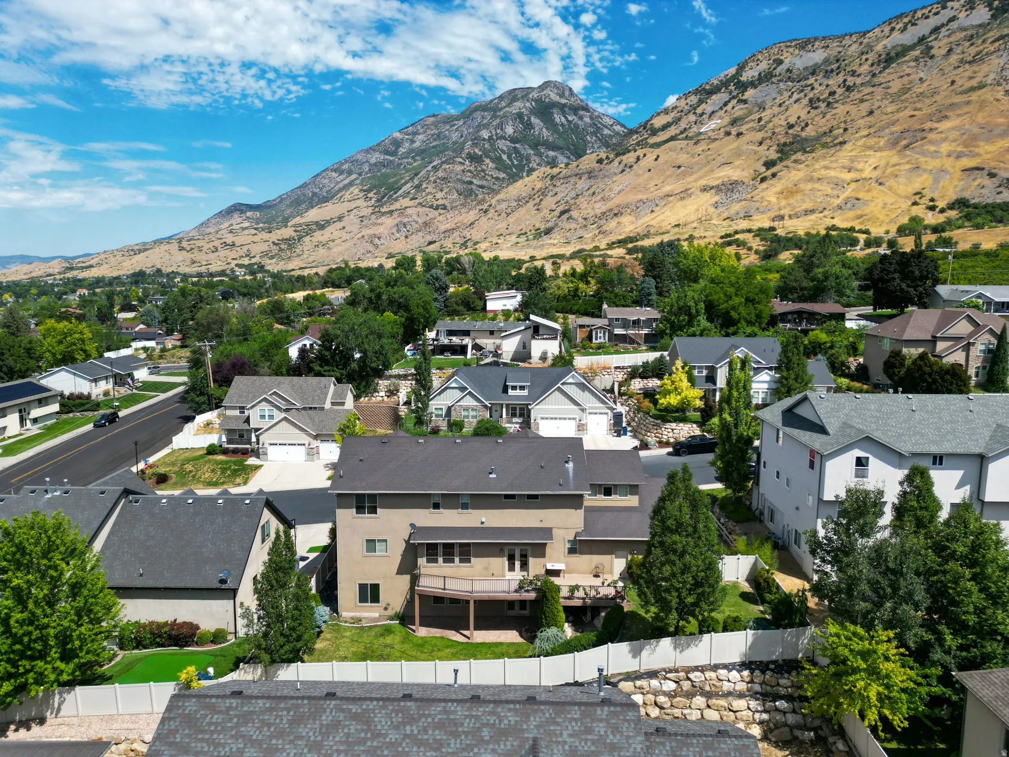 Elevated lot featuring a multi-level deck, mature landscaping, tiered stone retaining walls, and a white privacy fence