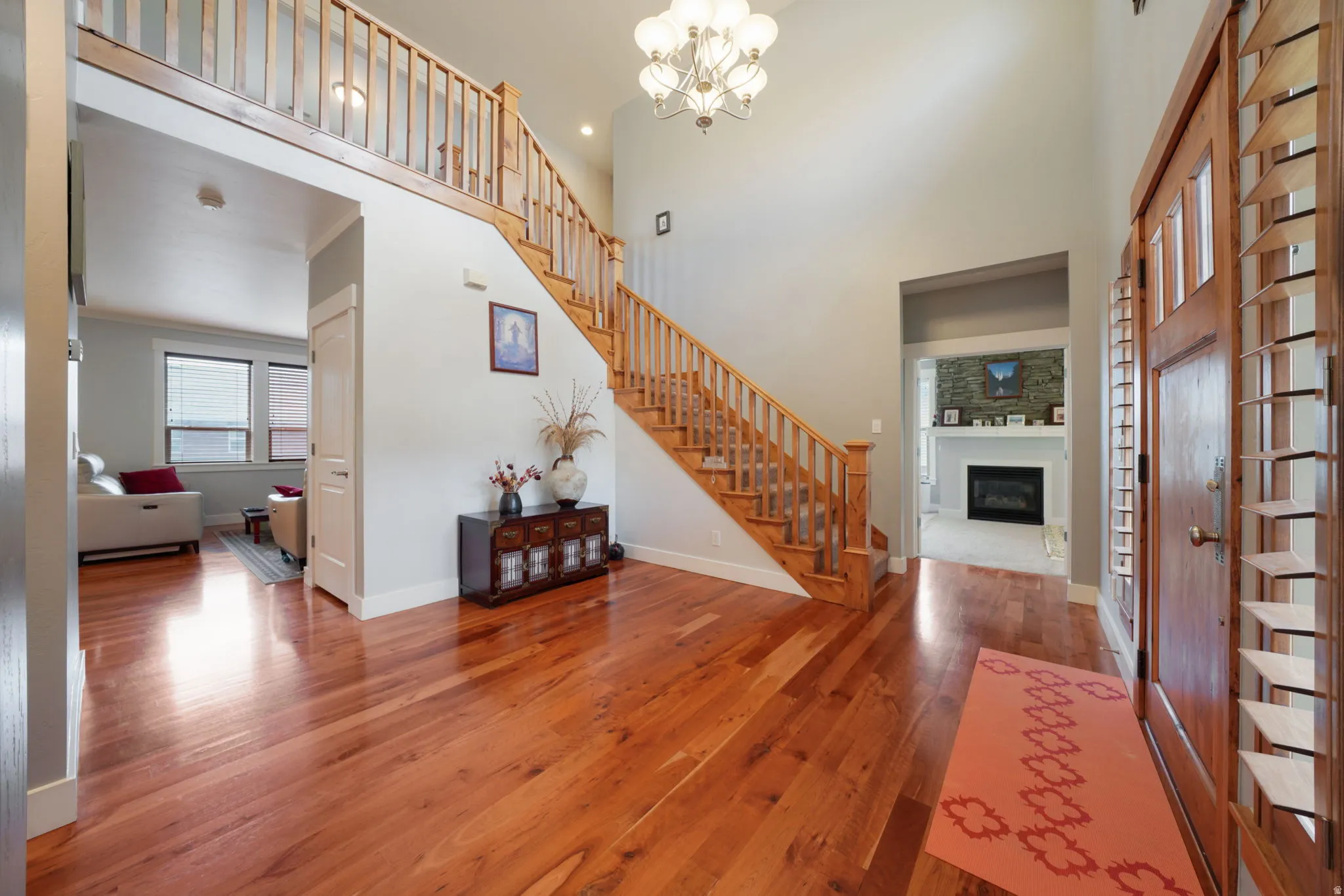 Spacious entryway featuring rich wood-finish flooring, a grand staircase with natural wood railings, and a double-height ceiling with a chandelier