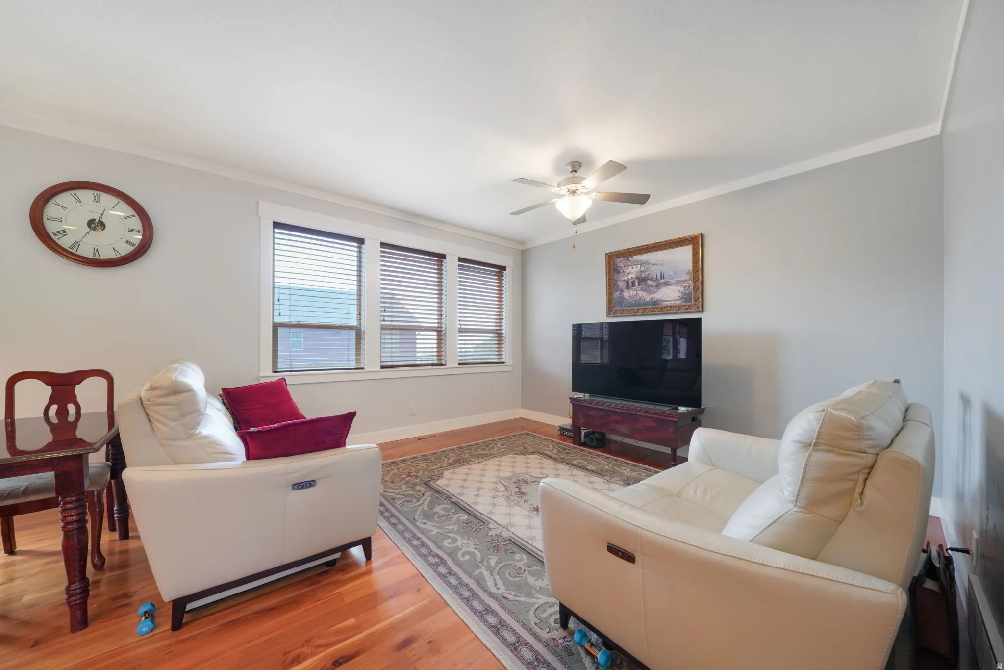 Living area featuring wood-finish flooring, a ceiling fan with integrated lighting, and multiple windows with blinds