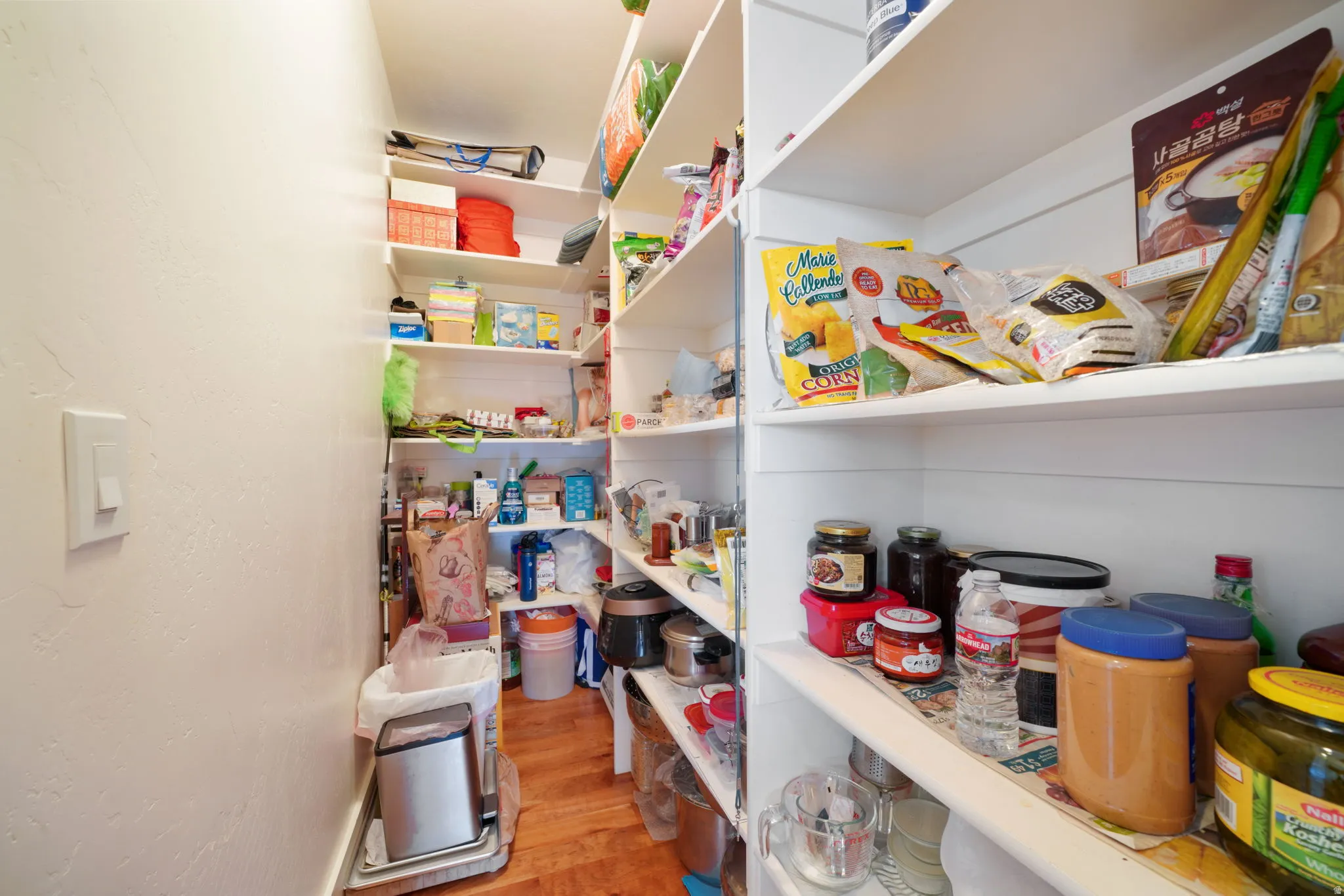 Spacious walk-in pantry featuring extensive built-in shelving, white painted walls, and wood-finish flooring