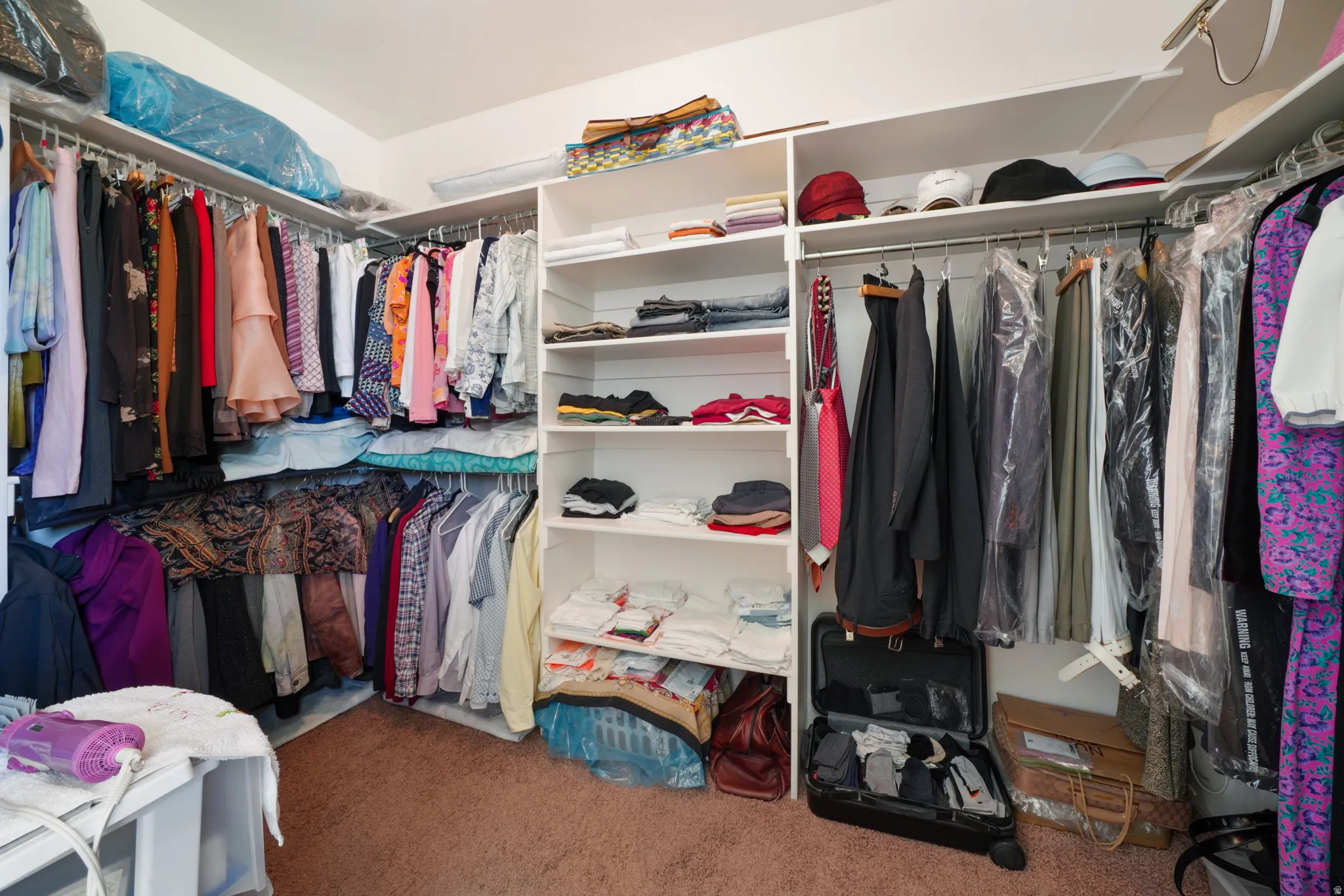 Spacious walk-in closet featuring white built-in shelving, multiple hanging rods, and recessed lighting