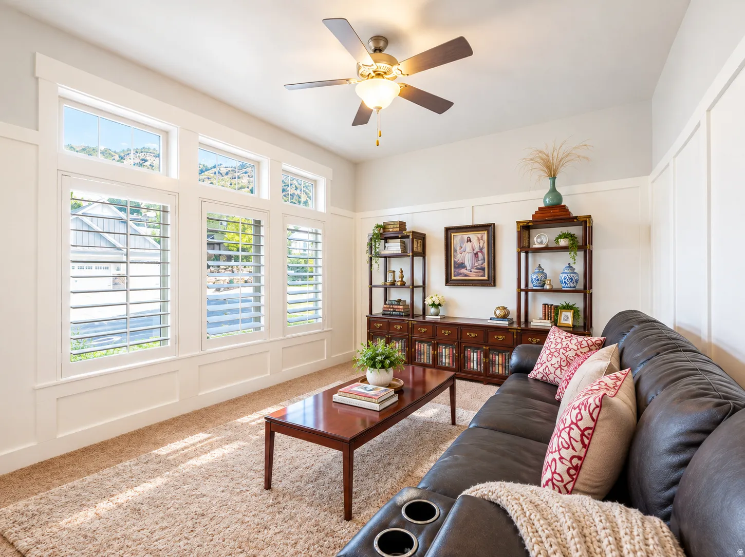 Recessed wall panels, multiple windows with plantation shutters, a ceiling fan with integrated lighting, and a built-in wall unit