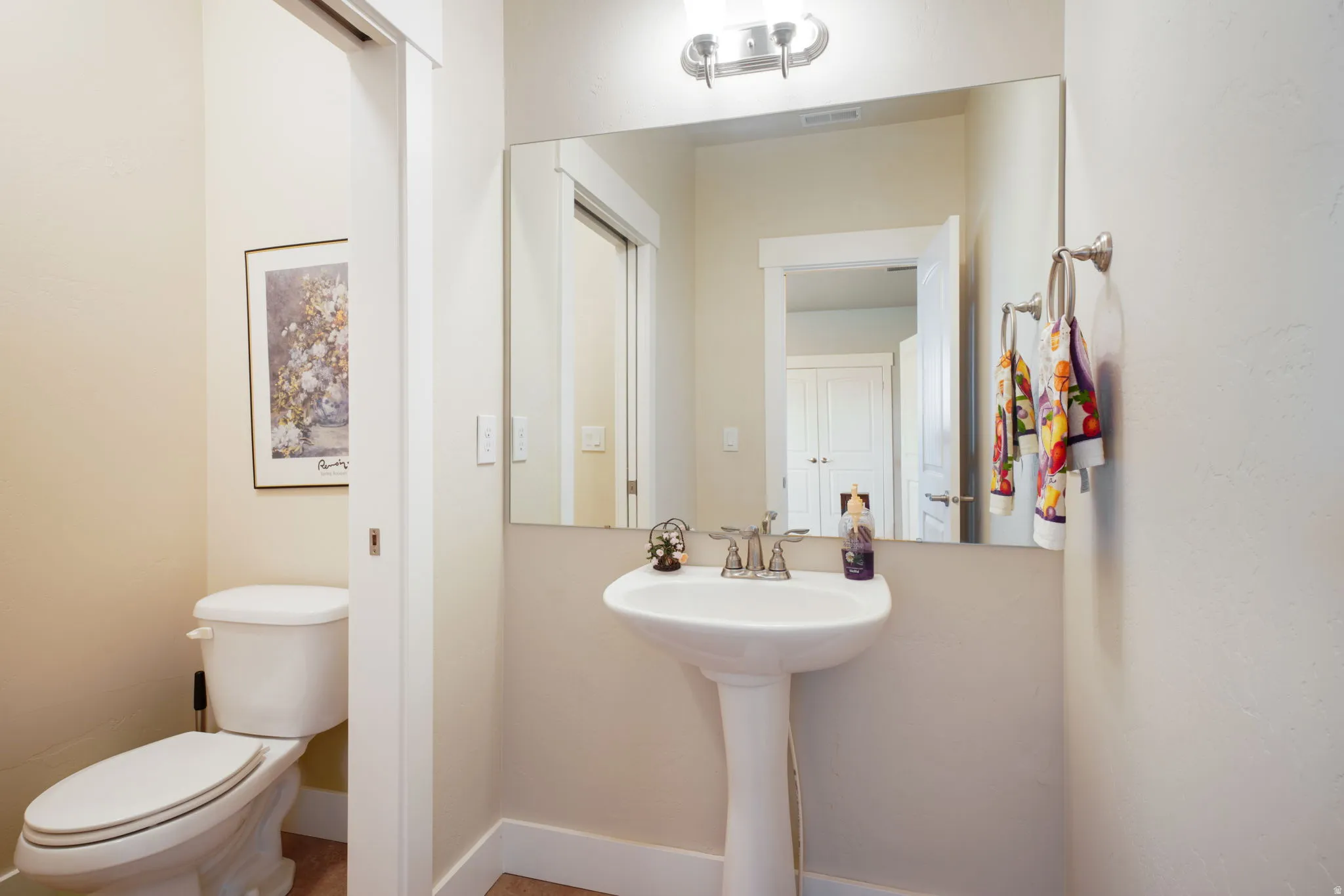 Pedestal sink with chrome faucet, large wall mirror, and overhead vanity lighting