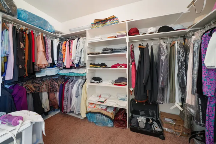 Spacious walk-in closet featuring white built-in shelving, multiple hanging rods, and recessed lighting