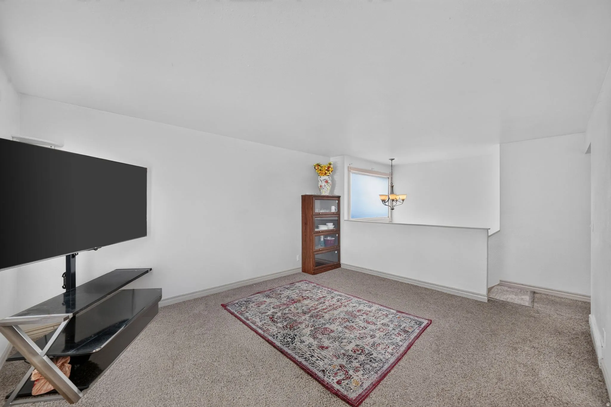 Carpeted room featuring a half-wall with a window and a multi-bulb chandelier