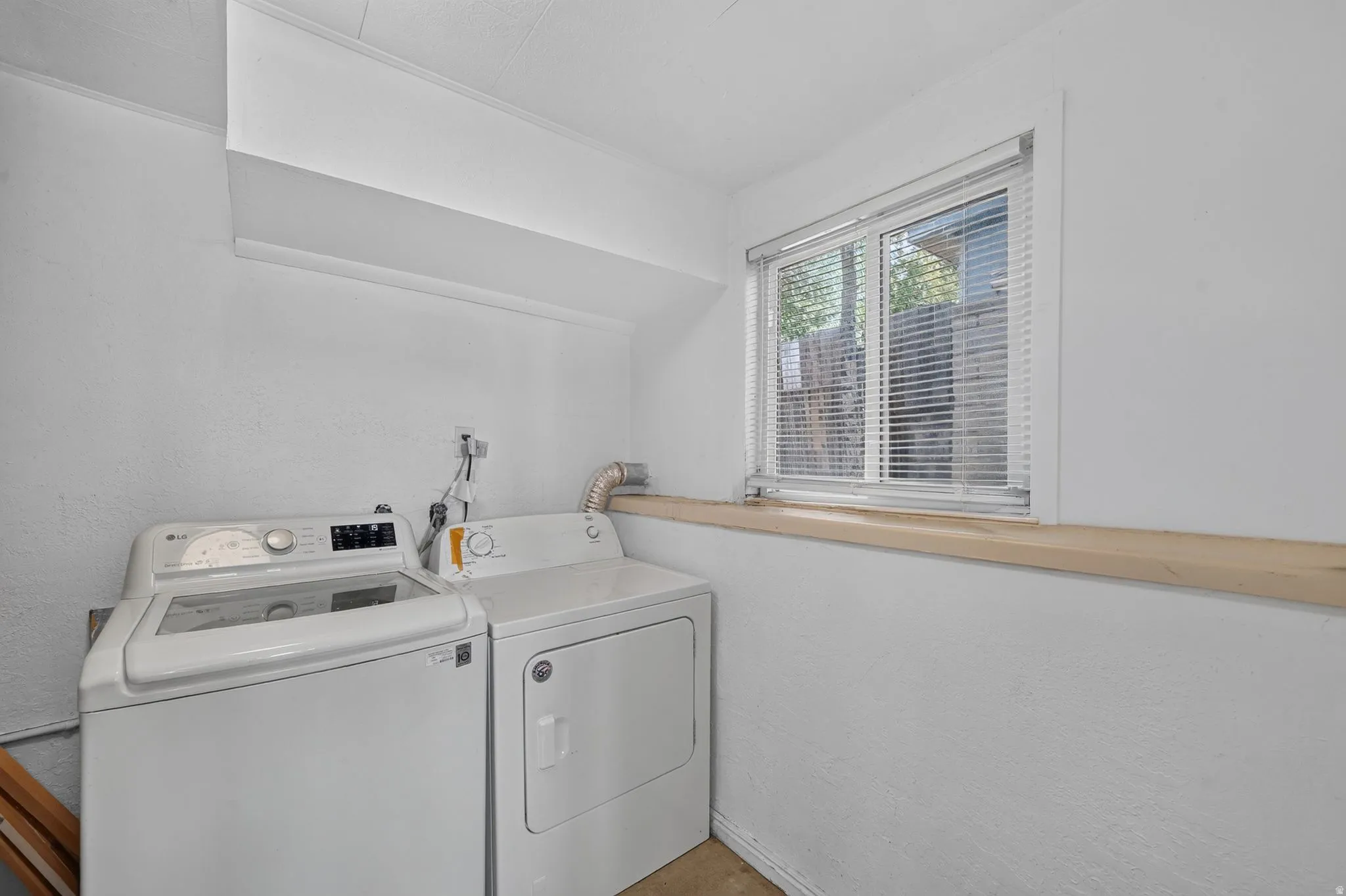 Laundry area featuring a window with blinds, white textured walls, and a light-toned wood shelf
