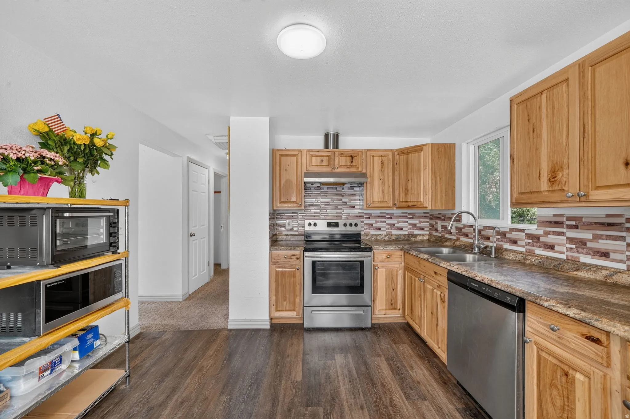 Kitchen featuring wood-finish flooring, natural wood cabinetry, stainless steel appliances, a mosaic tile backsplash, and a double basin sink