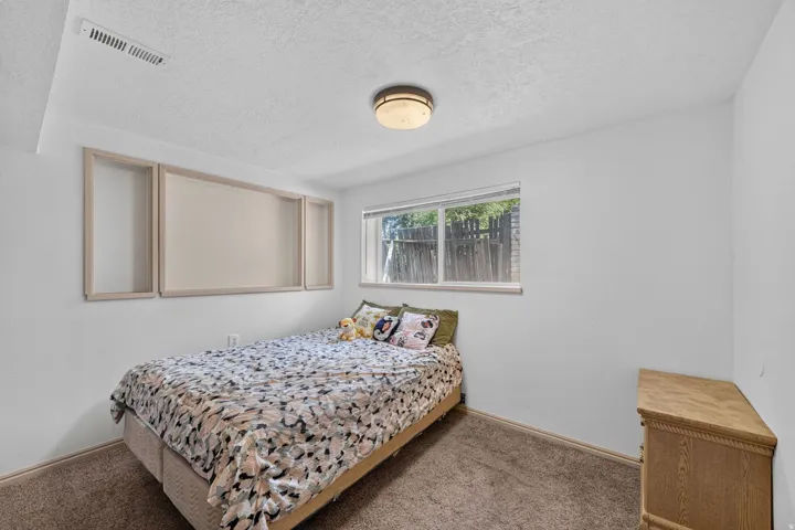 Bedroom featuring a window with exterior fencing visible, neutral carpet flooring, and white painted walls