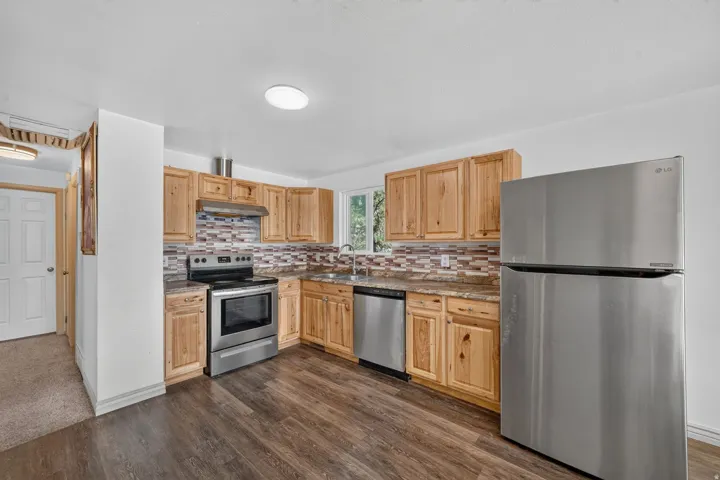 Kitchen featuring wood-finish flooring, natural wood cabinetry, stainless steel appliances, and a mosaic tile backsplash