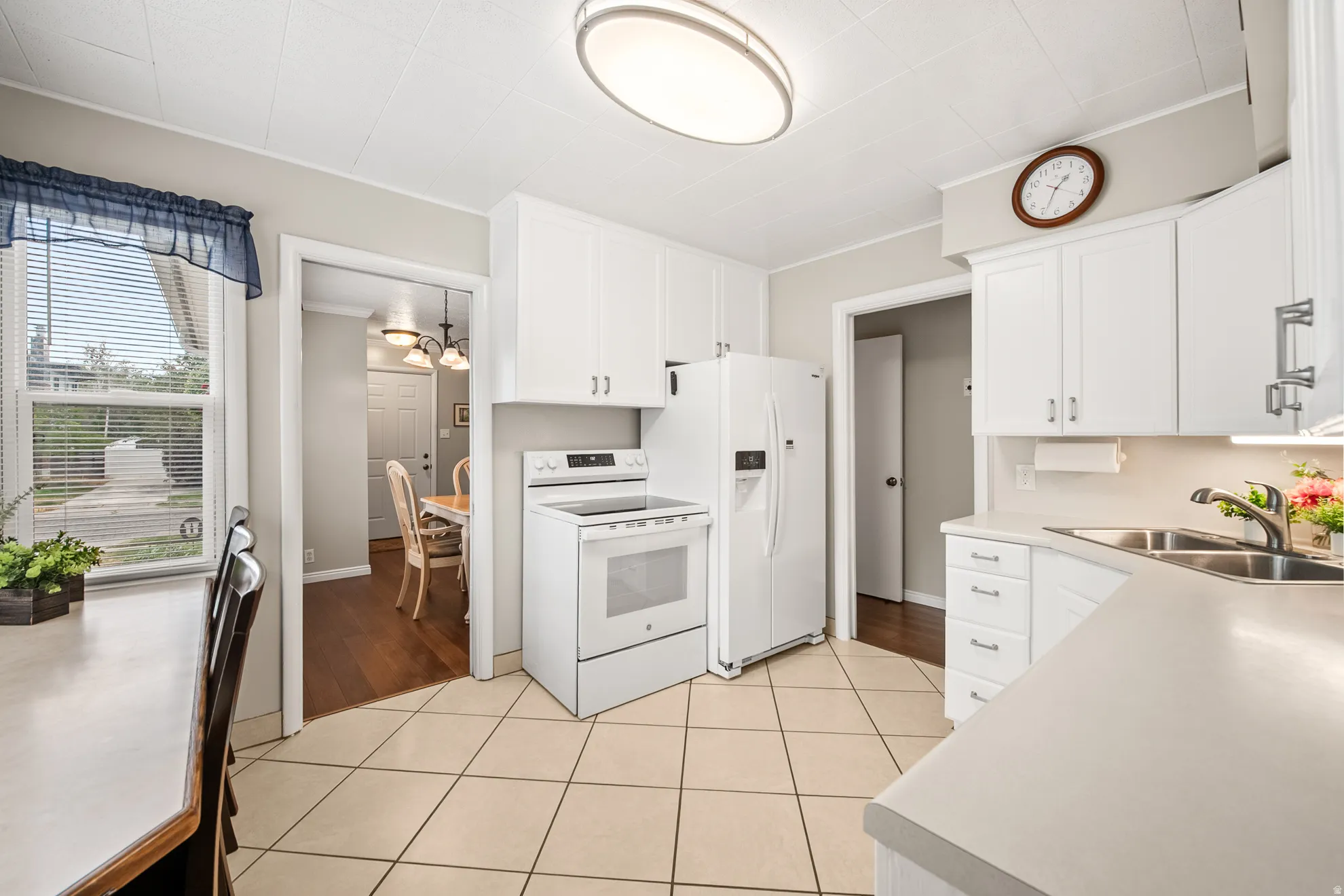 Kitchen featuring white cabinetry, white appliances, tile flooring, a window with blinds, and a double-basin stainless steel sink