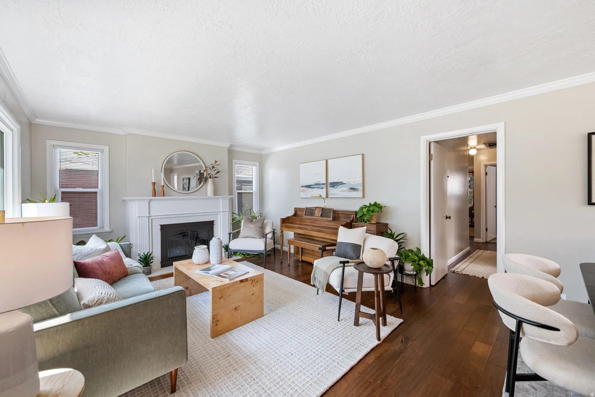 Living area featuring dark wood-finish flooring, a white mantel fireplace, multiple windows with white trim, and crown molding