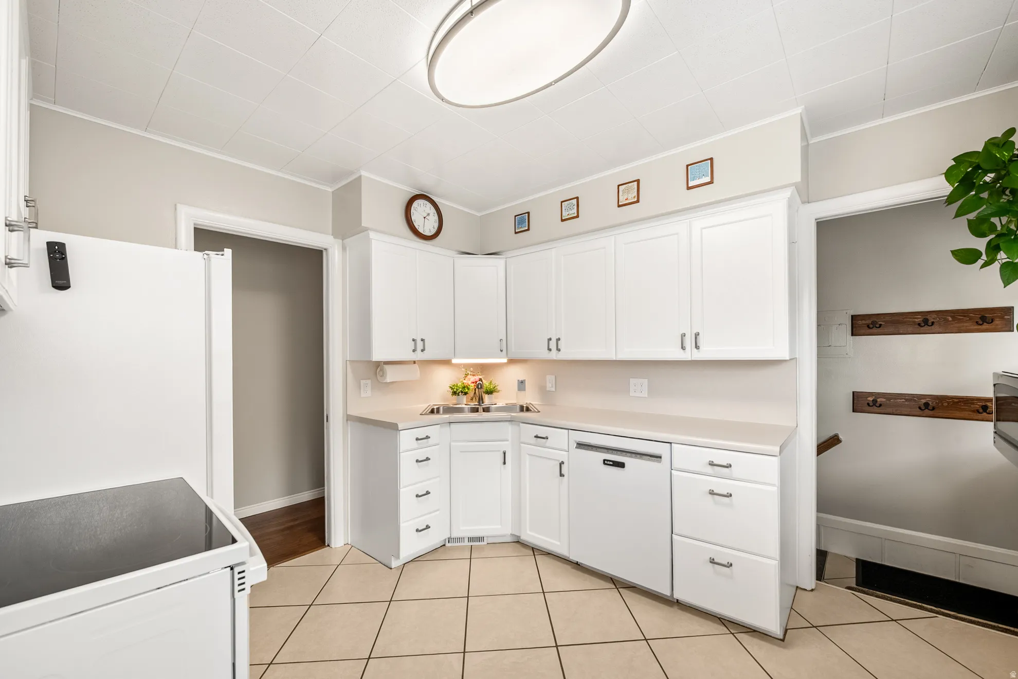 Bright kitchen featuring white cabinetry, light-toned countertops, a built-in dishwasher, and tile flooring