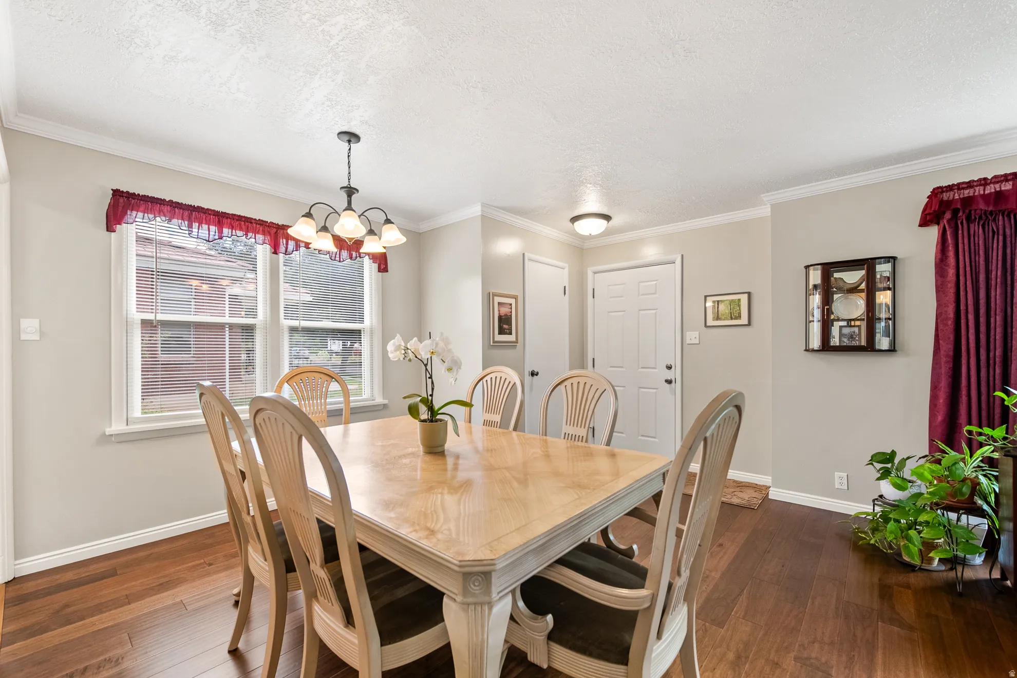 Dining area featuring wood-finish flooring, a multi-light chandelier, crown molding, and a white paneled entry door