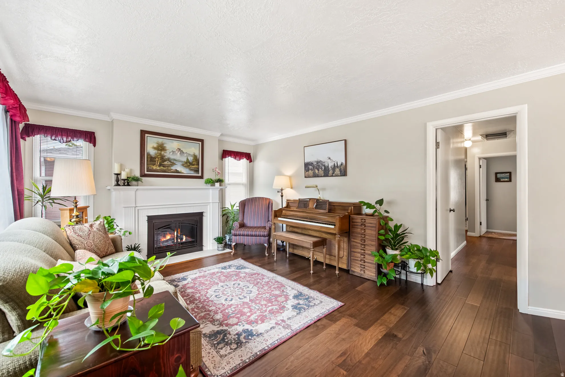 Living room featuring a prominent fireplace with a white mantel, rich wood-finish flooring, light neutral wall paint, and white crown molding