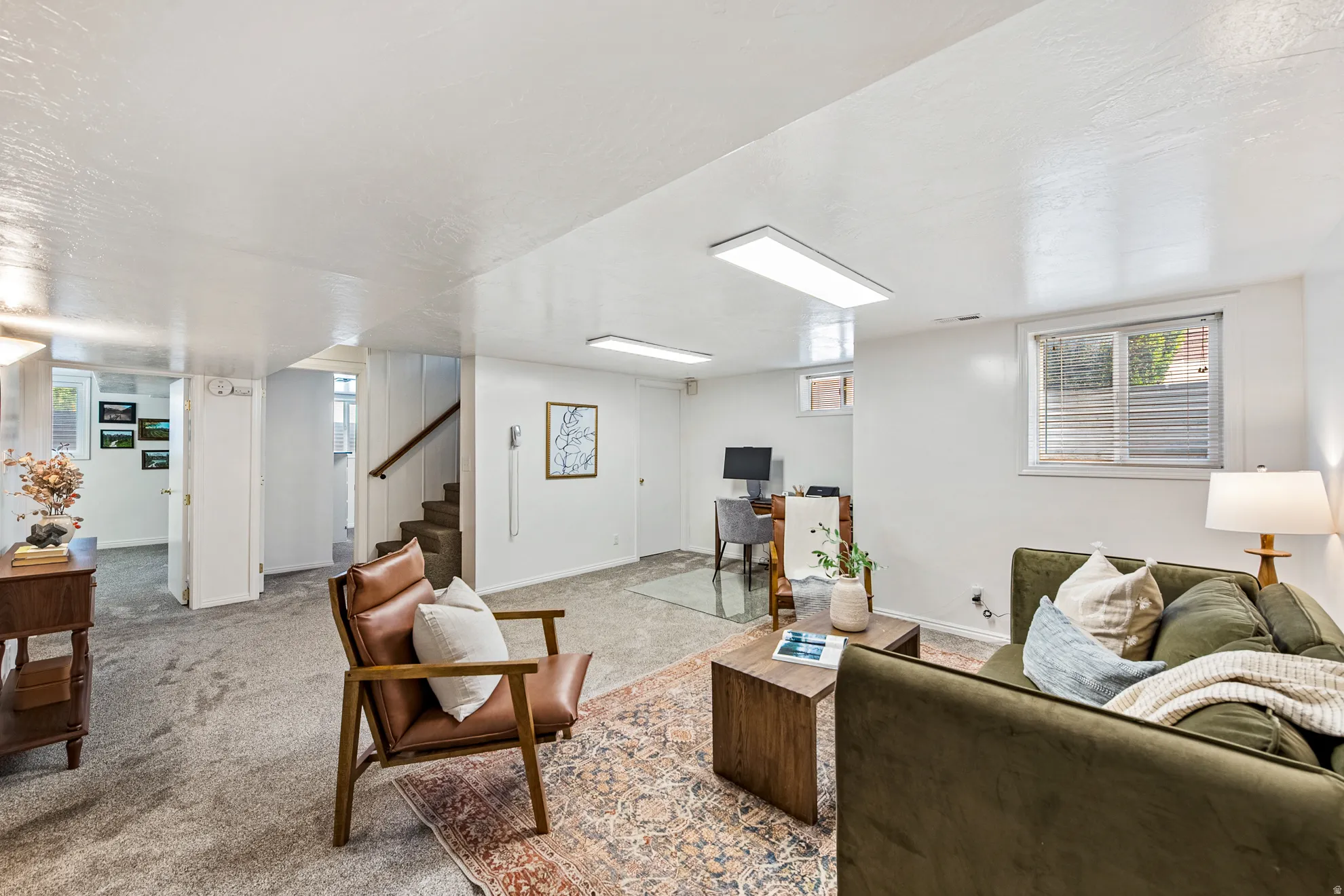 Carpeted living area with white walls, recessed lighting, and a staircase with a wooden handrail