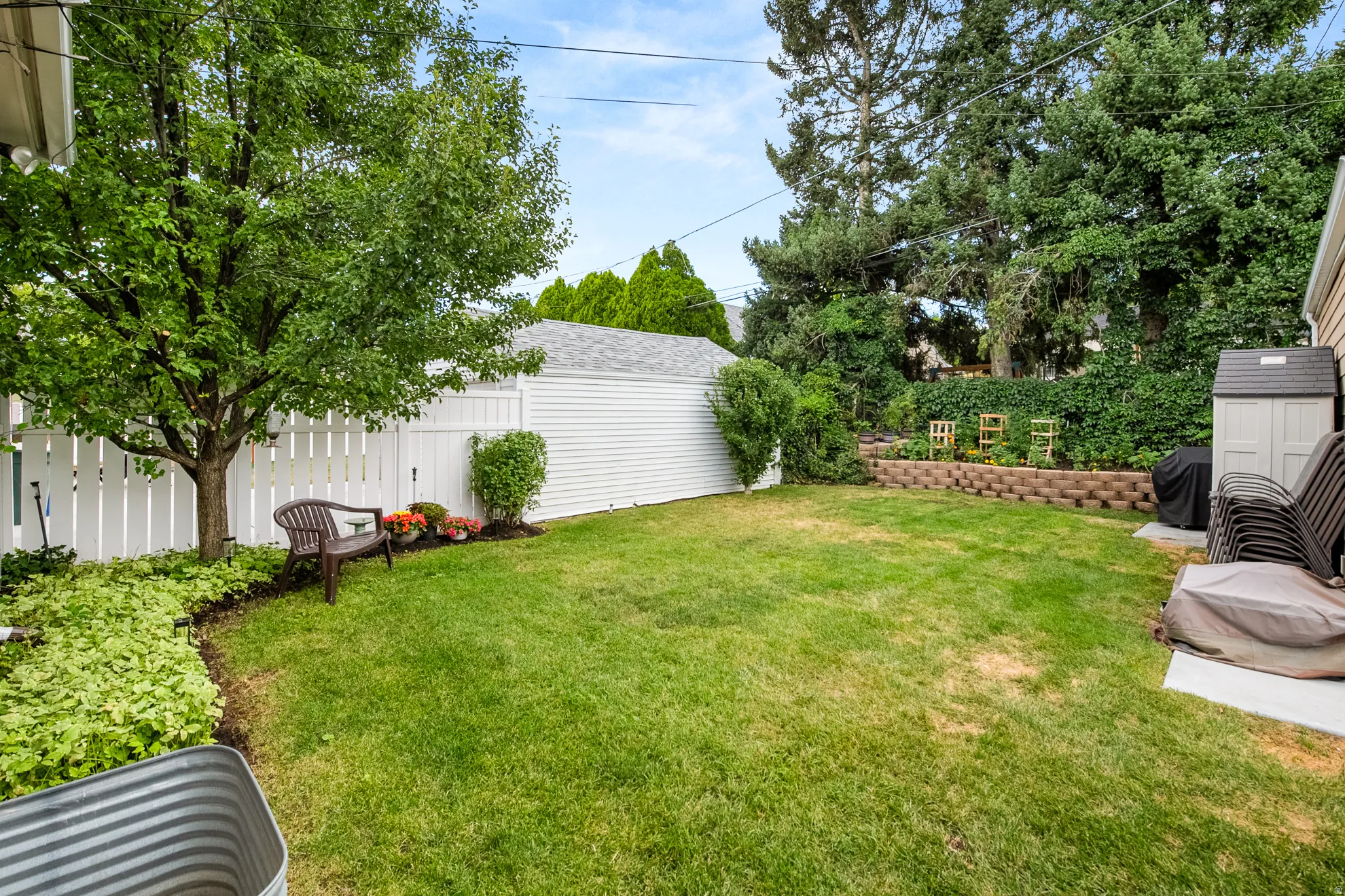 Private backyard featuring a manicured lawn, white picket fencing, mature trees, and a tiered retaining wall