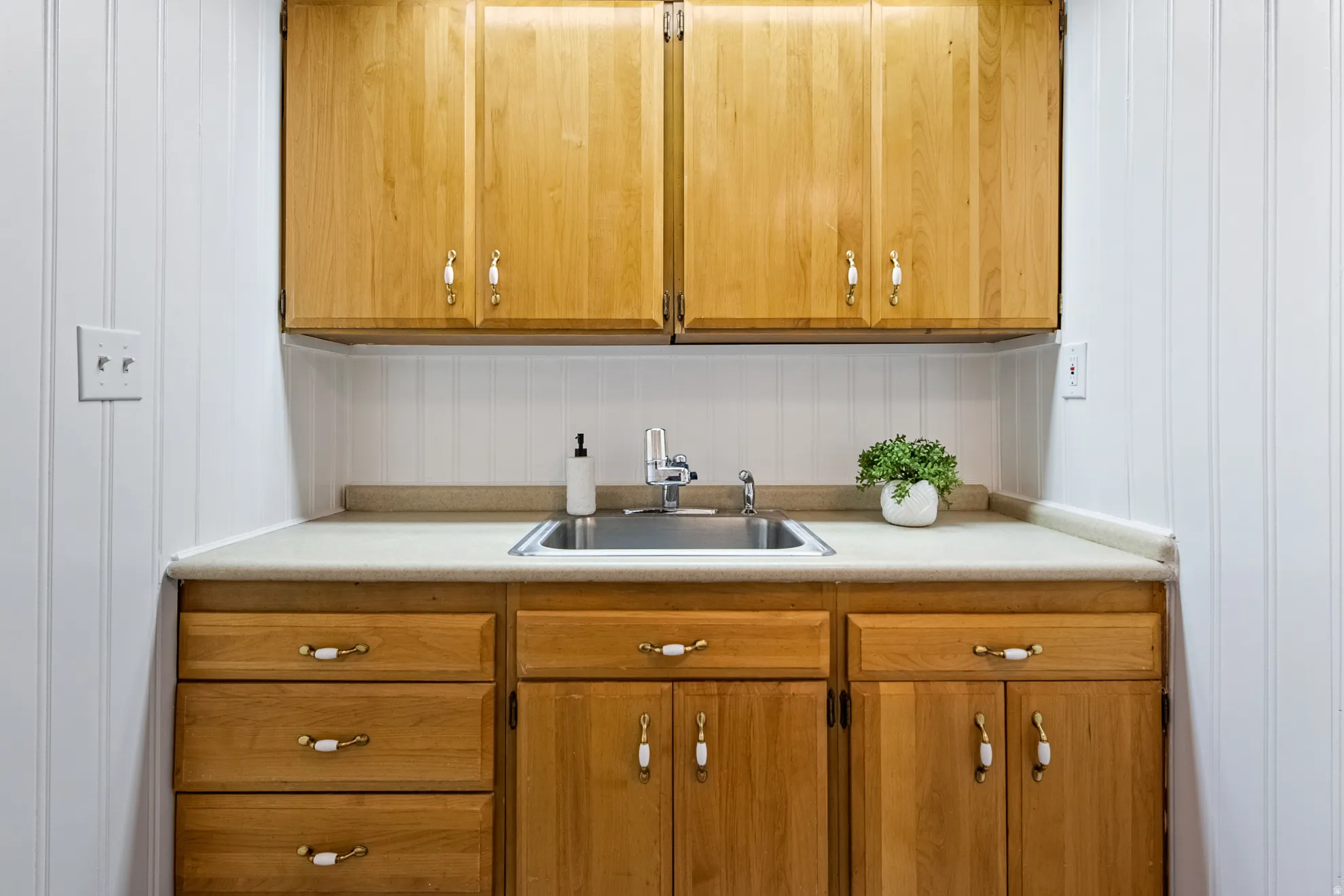 Light wood cabinetry with cream hardware, stainless steel sink, and light countertop