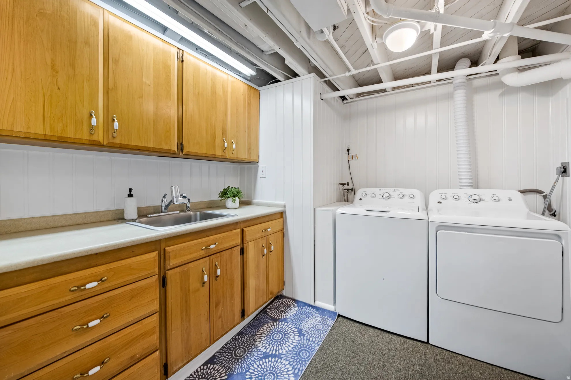 Utility room featuring wood cabinetry, a stainless steel sink, a countertop, and wall paneling