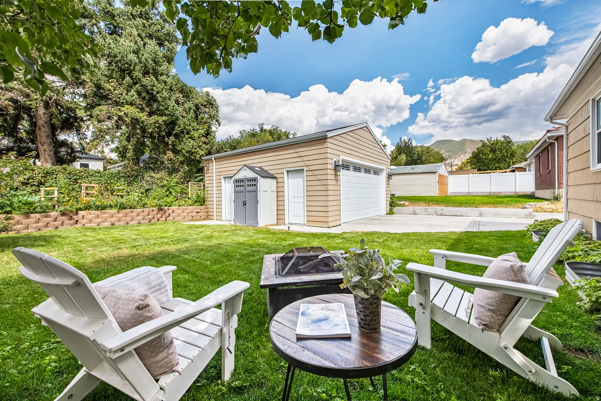 Expansive green lawn with a tiered retaining wall, detached garage, and an additional storage shed