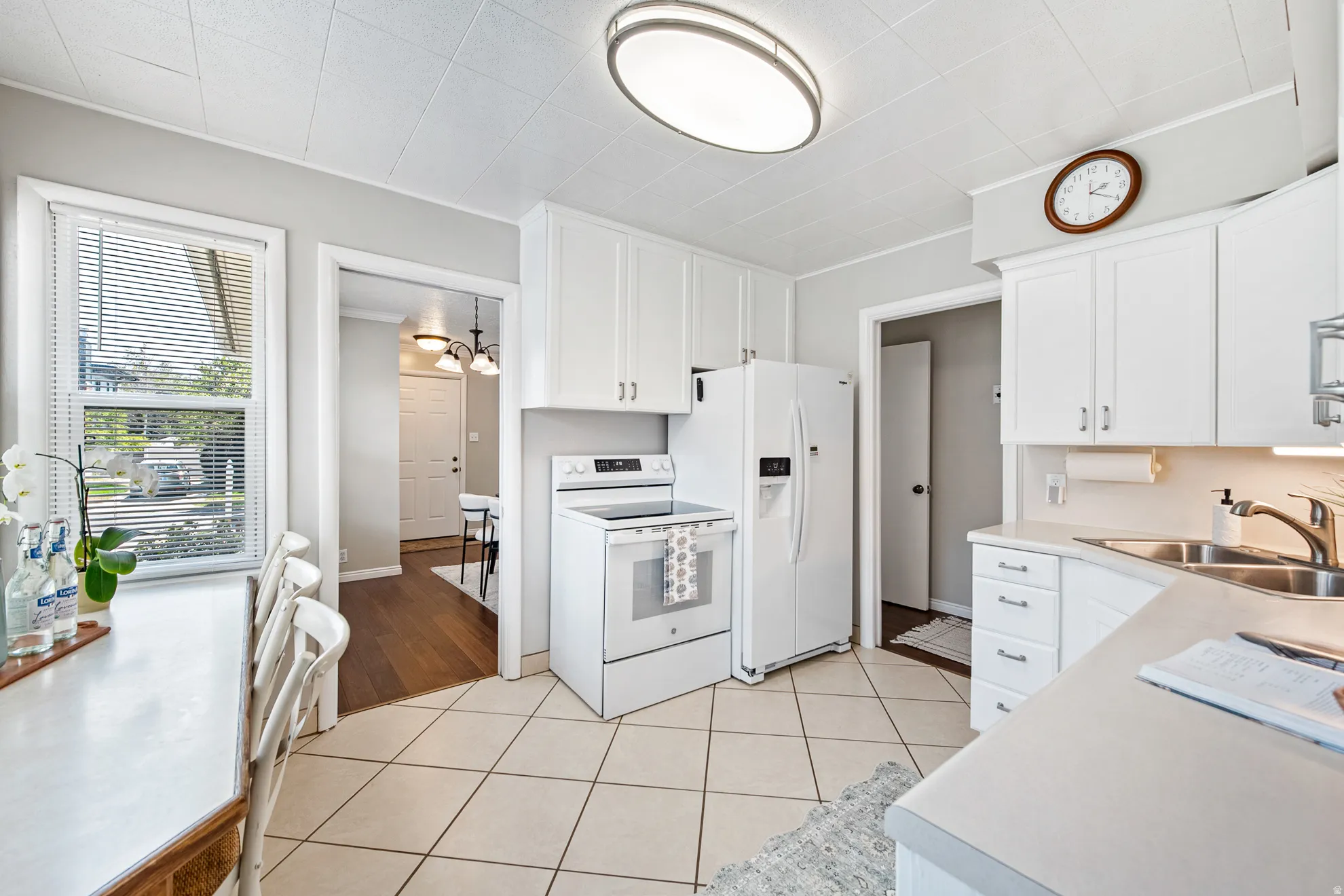 White cabinetry, tile flooring, window with blinds, recessed lighting, and a double basin sink