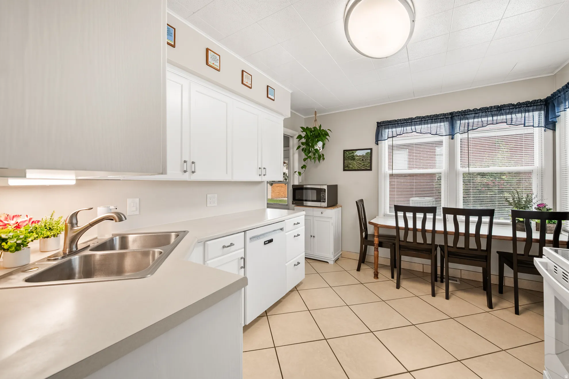 Kitchen featuring a double basin stainless steel sink, solid surface countertops, white cabinetry, integrated dishwasher, and tiled flooring