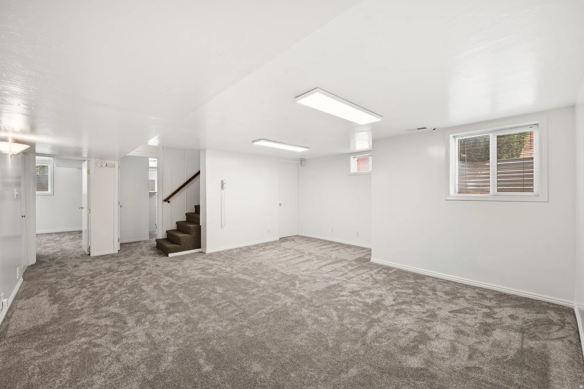 Spacious room featuring new gray carpeting, white walls, and bright overhead lighting