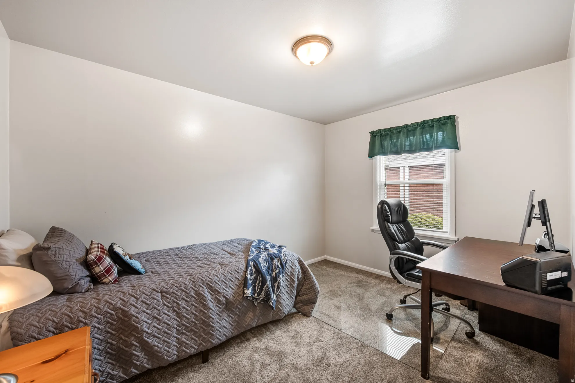 Carpeted room with a ceiling-mounted light fixture, white walls, and a window with a green valance