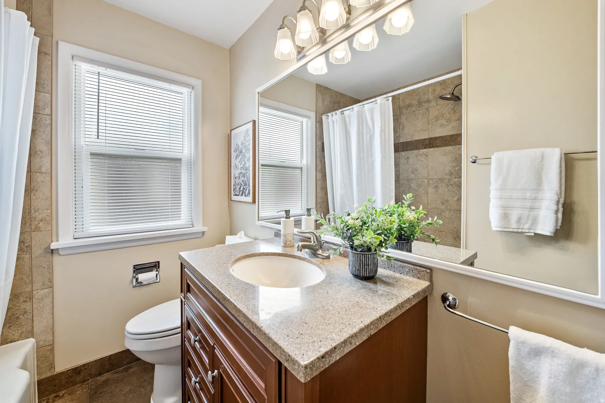 Bathroom featuring a wood-finish vanity with a light-colored countertop, an undermount sink, and a large wall mirror