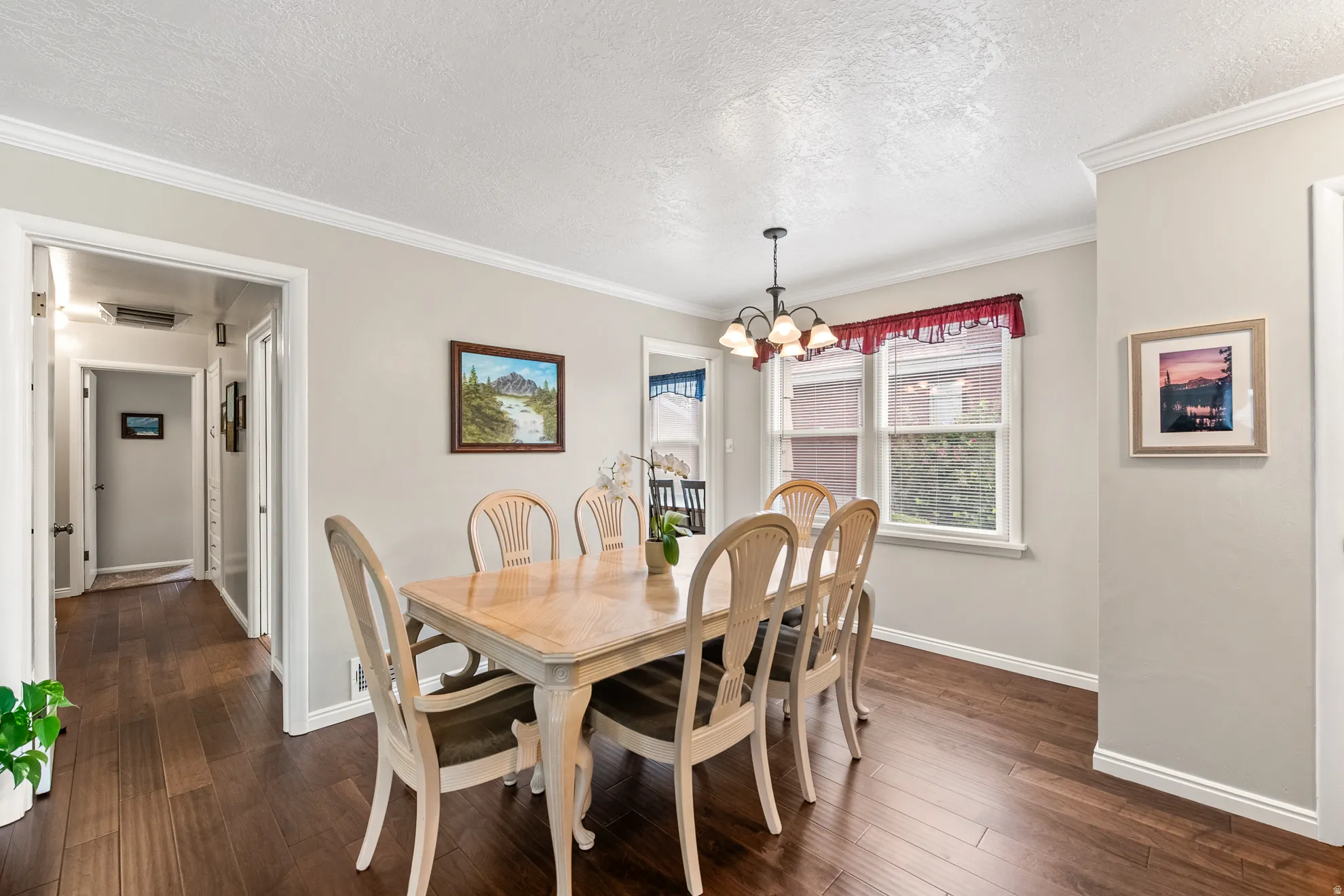 Dining area featuring dark wood-finish flooring, two windows with white trim, a multi-bulb chandelier, crown molding, and baseboards