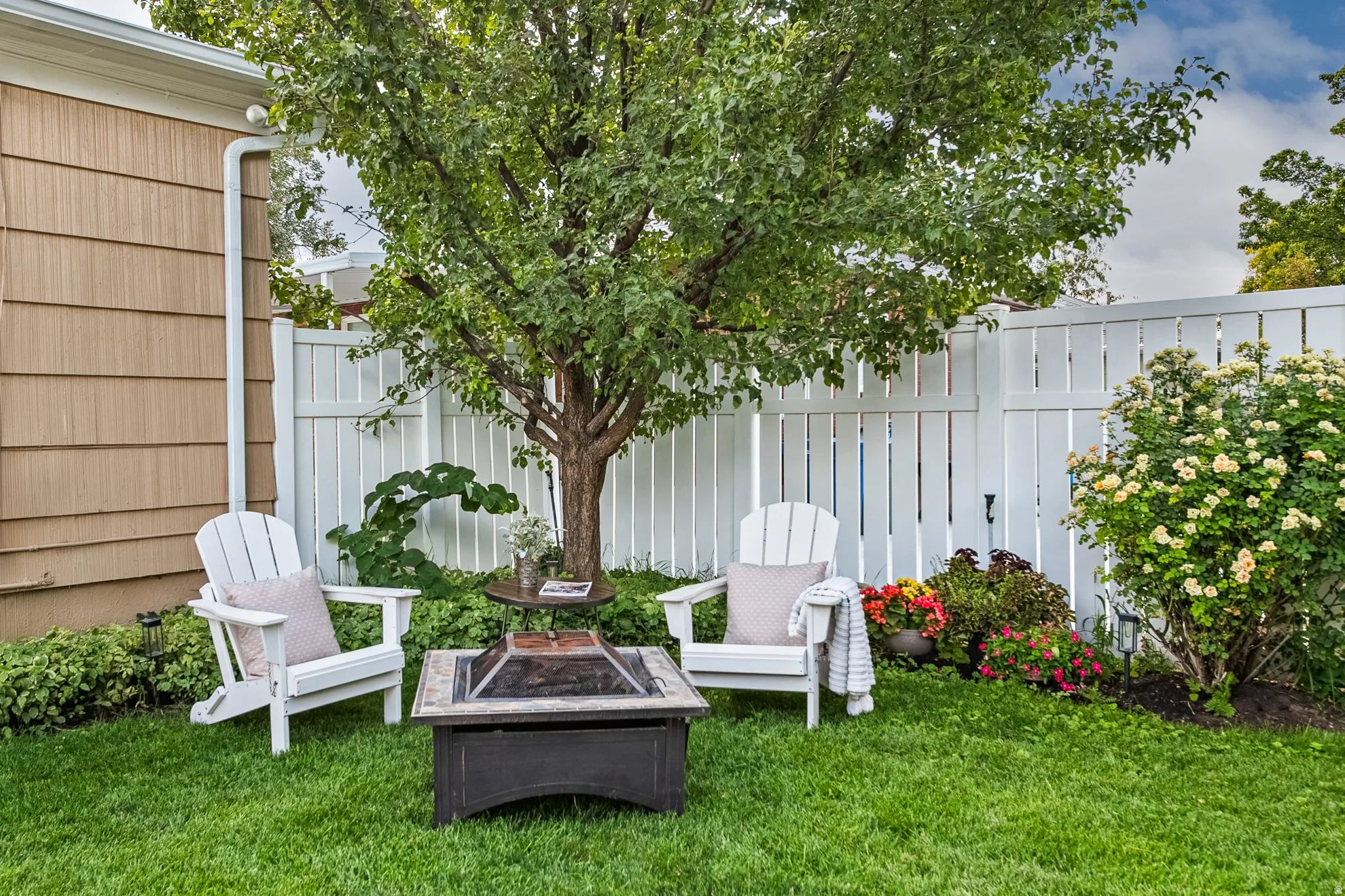 Private backyard space featuring a white privacy fence, mature tree, and lush green lawn