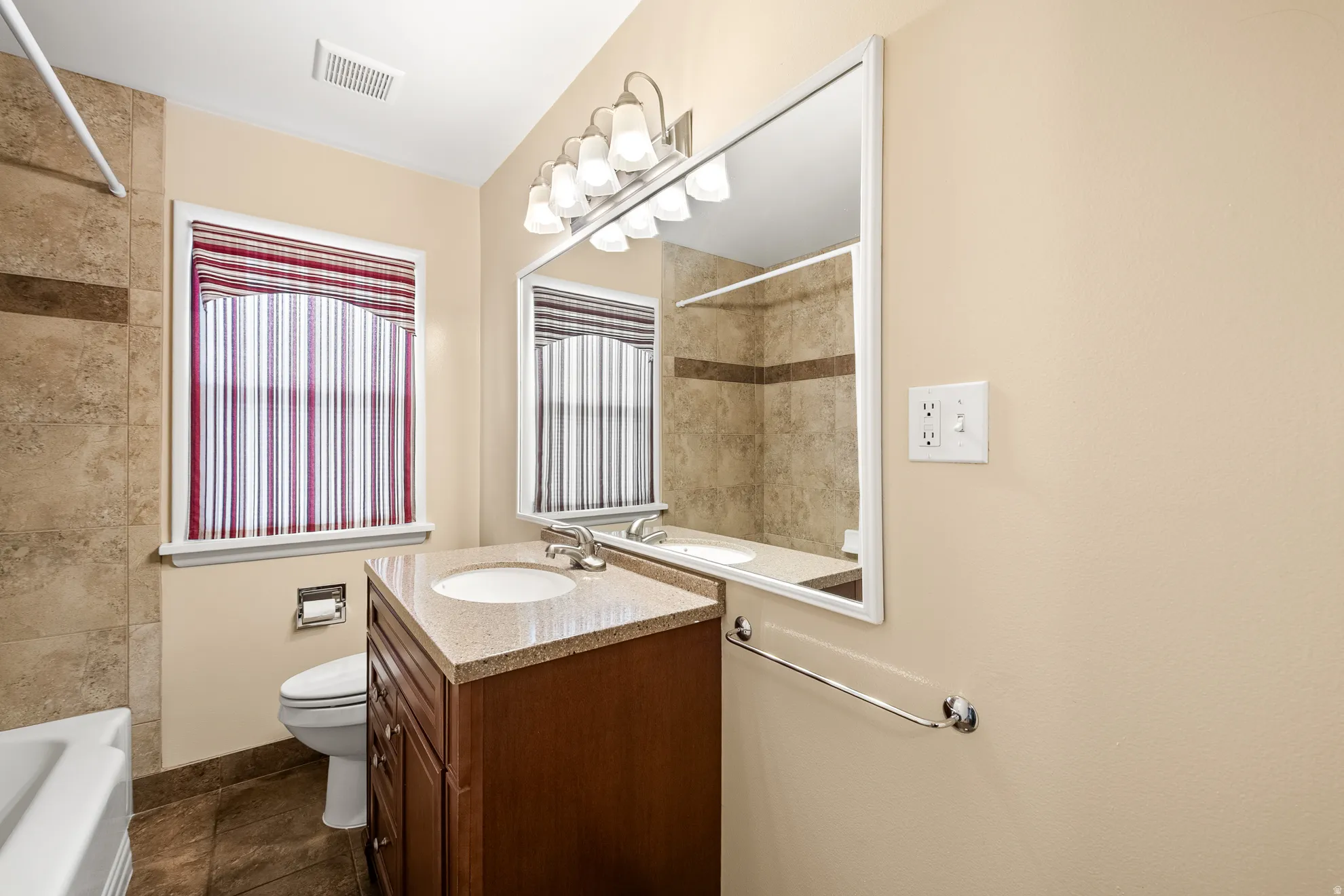 Bathroom featuring a vanity with a light-toned countertop and integrated sink, a rectangular mirror with a white frame, and a wall-mounted light fixture with five frosted glass shades