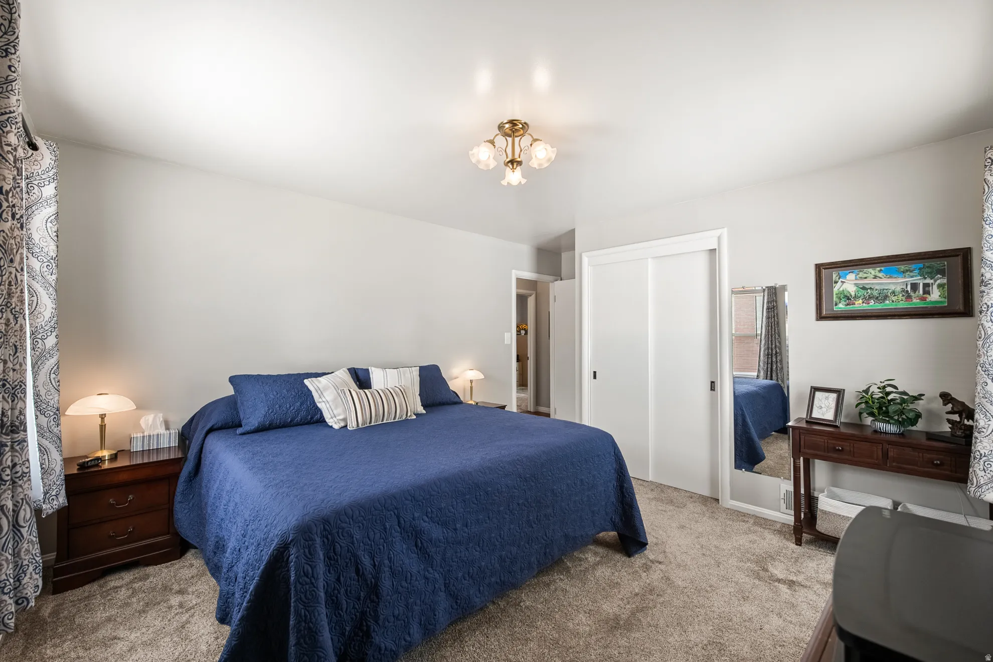 Spacious bedroom featuring light neutral wall tones, carpet flooring, a brass-finish ceiling light fixture, and a built-in sliding door closet