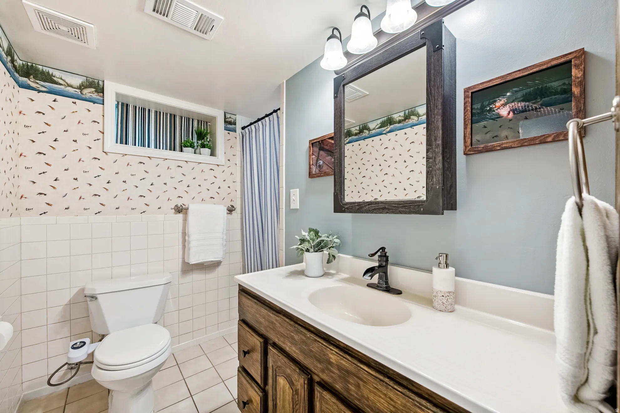 Vanity with a single basin sink and dark-finish faucet, framed mirror with integrated lighting, and white tile wainscoting