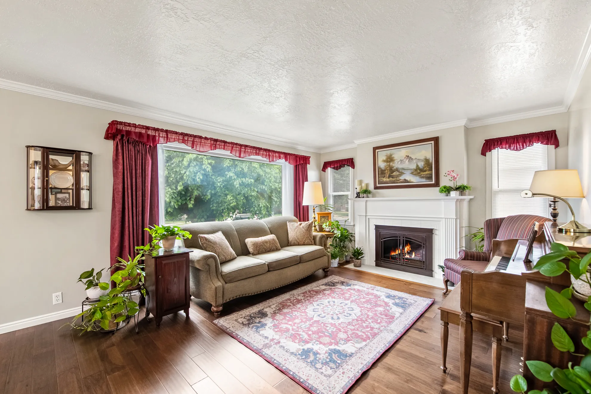 Living room featuring wood-finish flooring, a white mantel fireplace, crown molding, and a large picture window