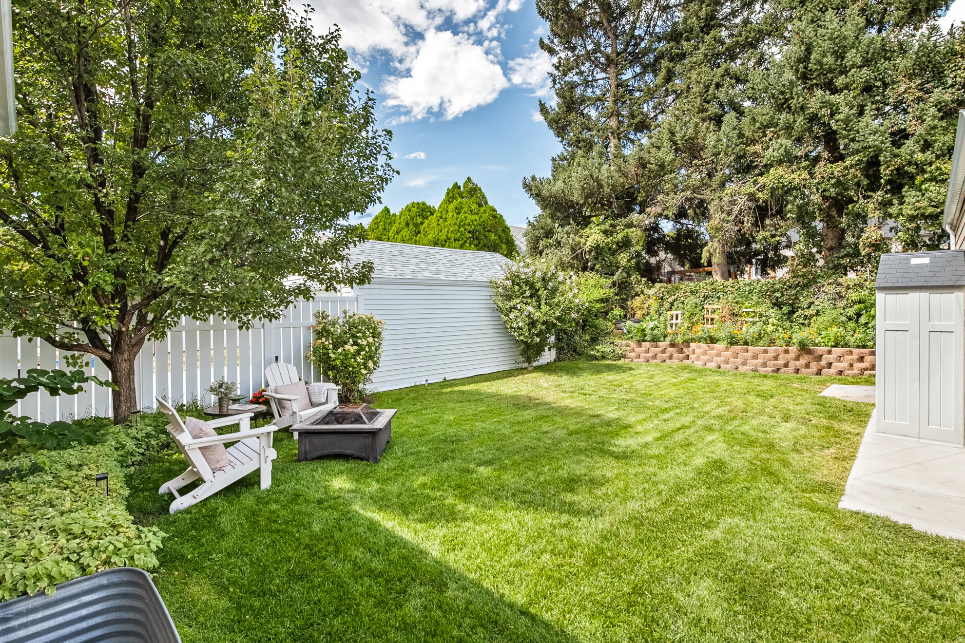 Expansive backyard featuring a manicured lawn, established trees, a white picket fence, a storage shed, and a tiered garden bed