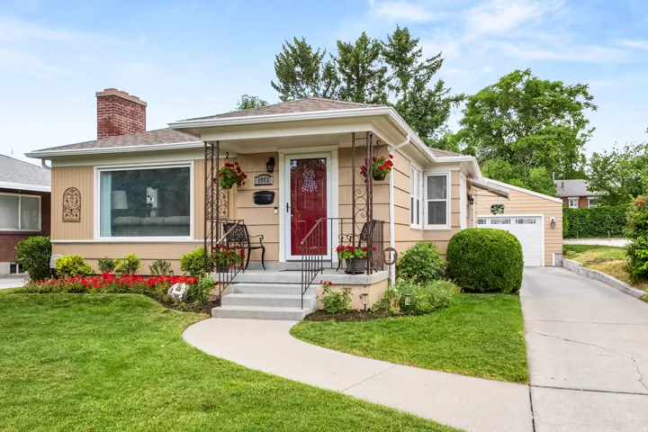Front exterior showcasing a covered porch with decorative railing, a red entry door, and light-toned siding