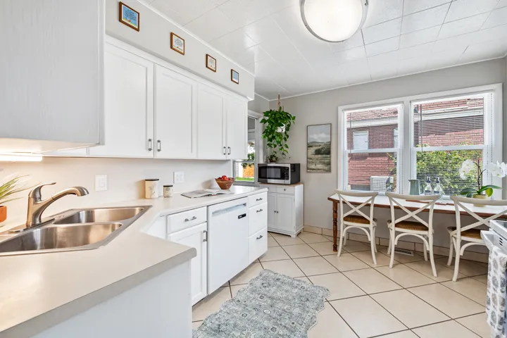 White cabinetry, solid surface countertops, dual basin stainless steel sink, and tile flooring