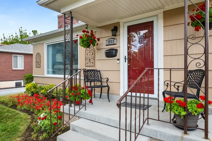 Front porch featuring concrete steps, wrought iron railings, a red entry door, and tan siding