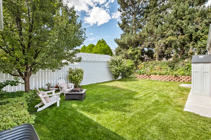 Expansive backyard featuring a manicured lawn, established trees, a white picket fence, a storage shed, and a tiered garden bed