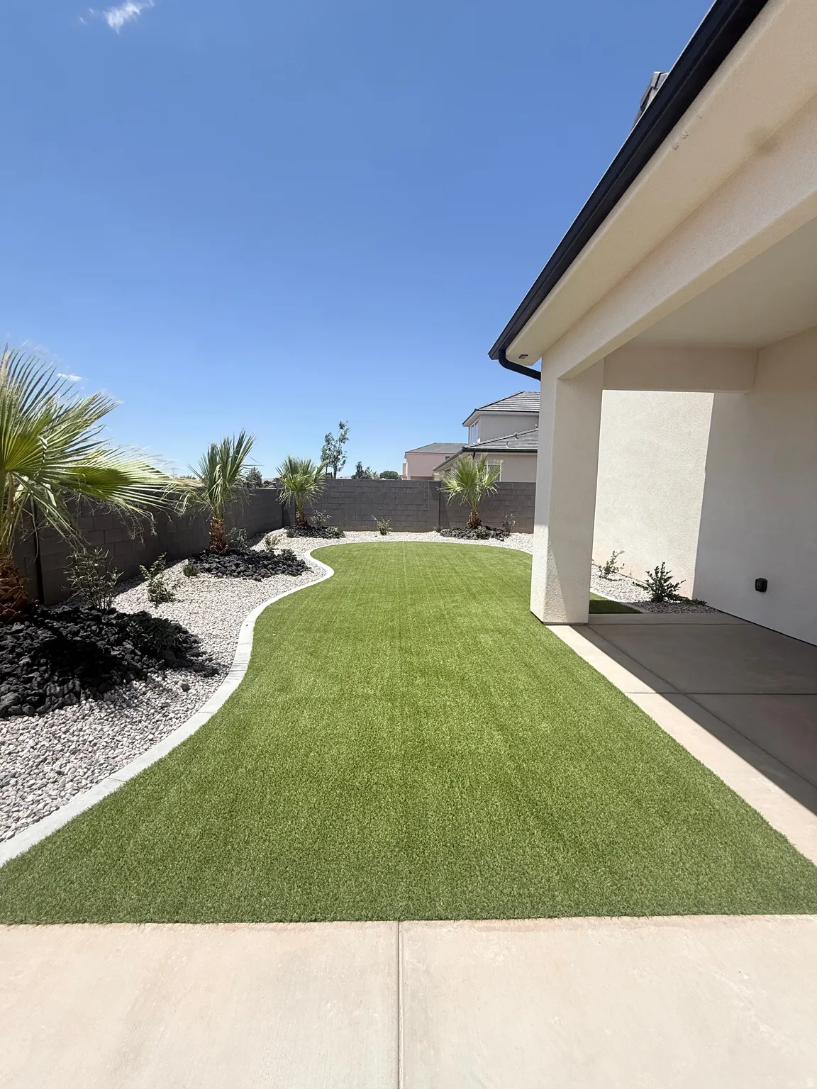 Expansive backyard featuring artificial turf, decorative rock landscaping, mature desert plantings, and a concrete patio