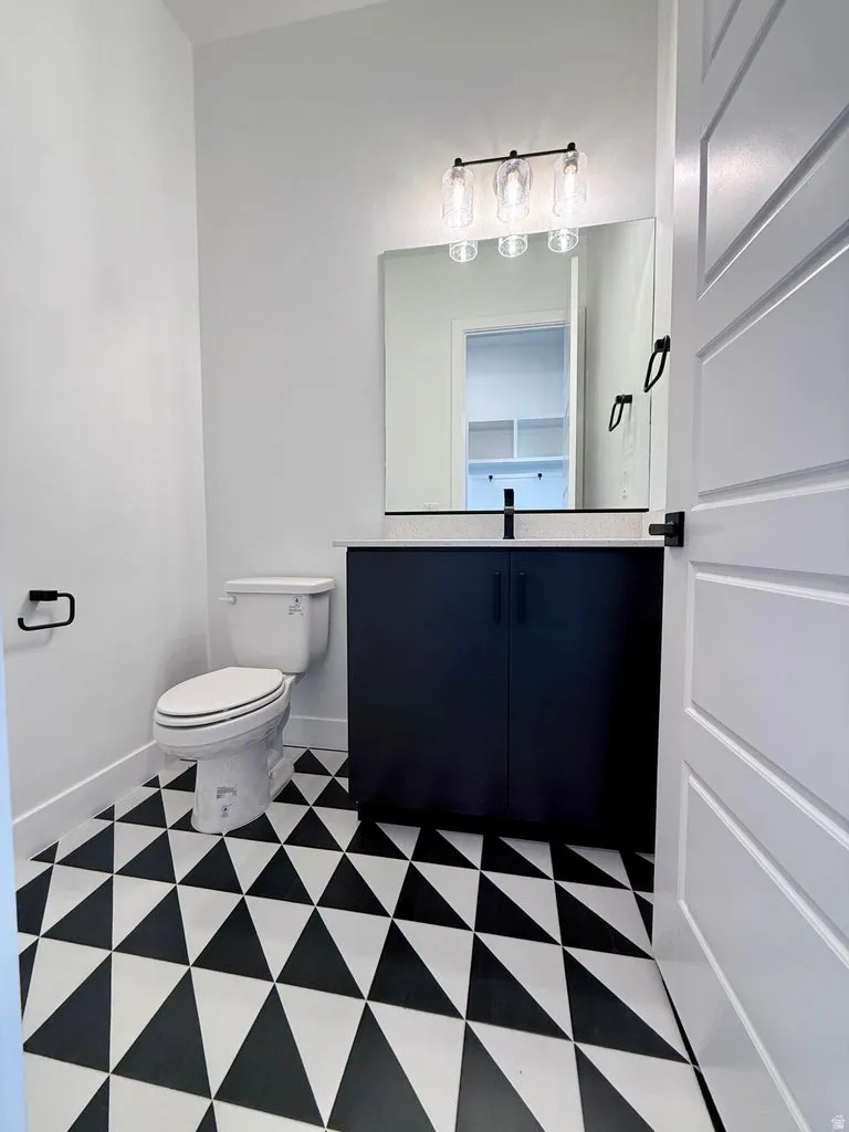 Bathroom featuring a geometric black and white tile floor, a dark wood-finish vanity with a light-colored countertop, and a contemporary three-light vanity fixture