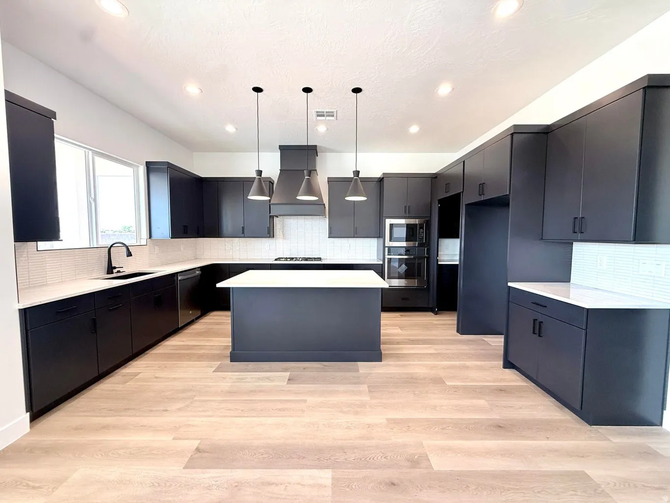 Spacious kitchen featuring dark cabinetry, an expansive center island with a white countertop, stainless steel double ovens, and wood-finish flooring