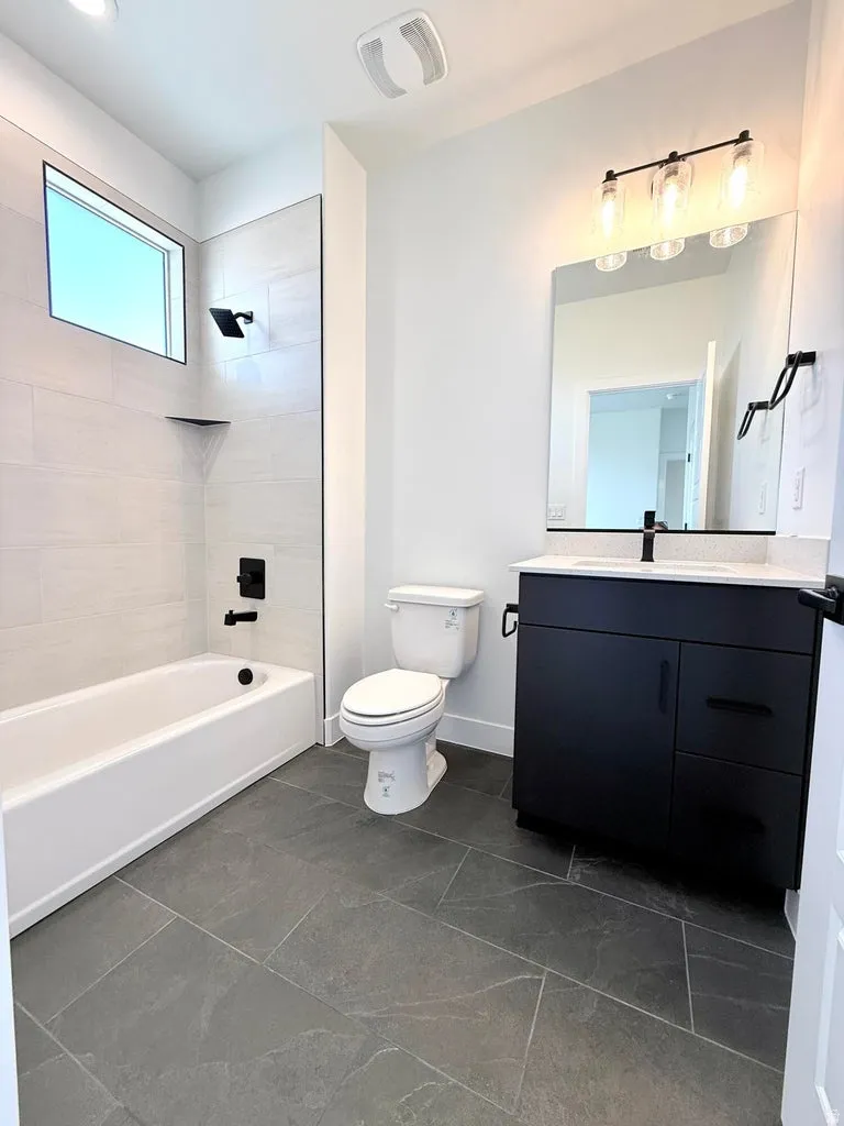 Modern bathroom featuring dark gray floor tiling, a white tub with matte black fixtures, and a sleek black vanity with a white countertop