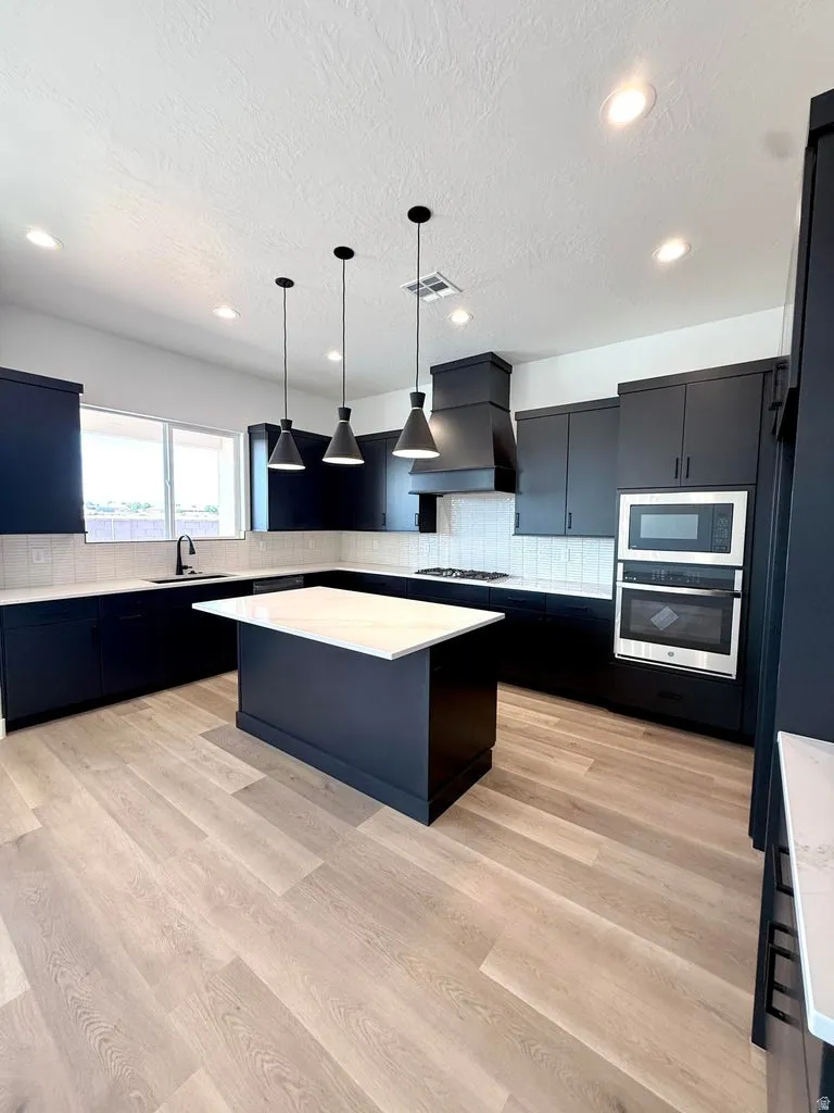 Modern kitchen featuring dark cabinetry, light countertops, wood-finish flooring, a central island, and stainless steel appliances