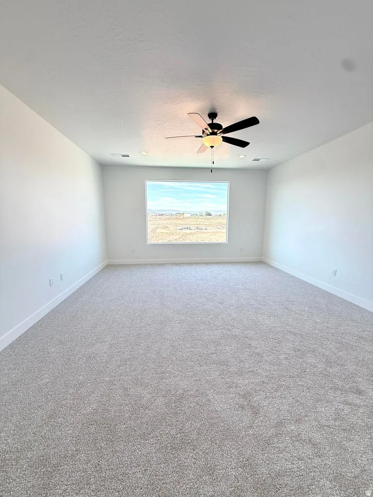 Spacious room featuring a large window, light-colored carpet flooring, white painted walls, a ceiling fan, and recessed lighting