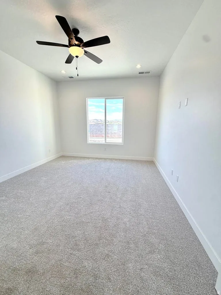 Spacious room featuring neutral carpeting, white walls, a large window, a ceiling fan, and recessed lighting