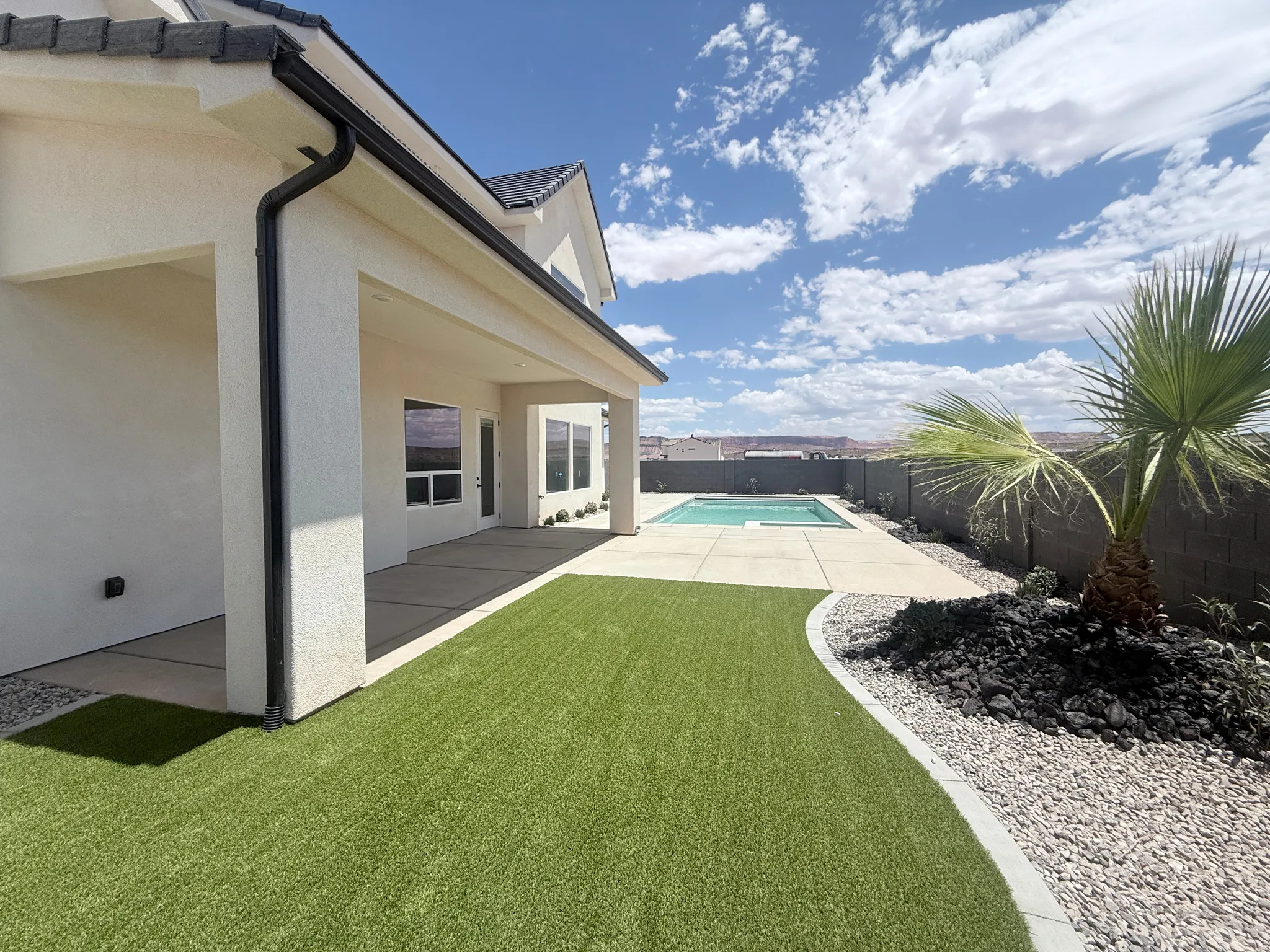 Backyard oasis featuring a swimming pool, covered patio, artificial turf, and desert landscaping with a palm tree