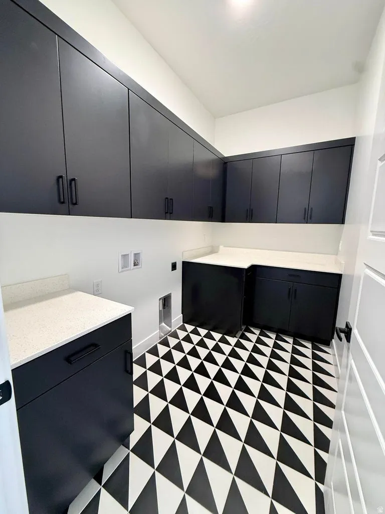 Laundry room featuring a geometric black and white floor tile pattern, extensive dark cabinetry, light-toned countertops, and bright white walls
