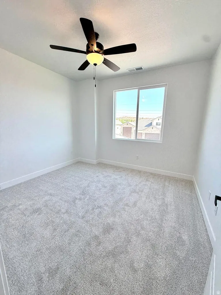 Spacious room featuring light gray carpeting, crisp white walls, a large window, a ceiling fan with integrated lighting, and white baseboards