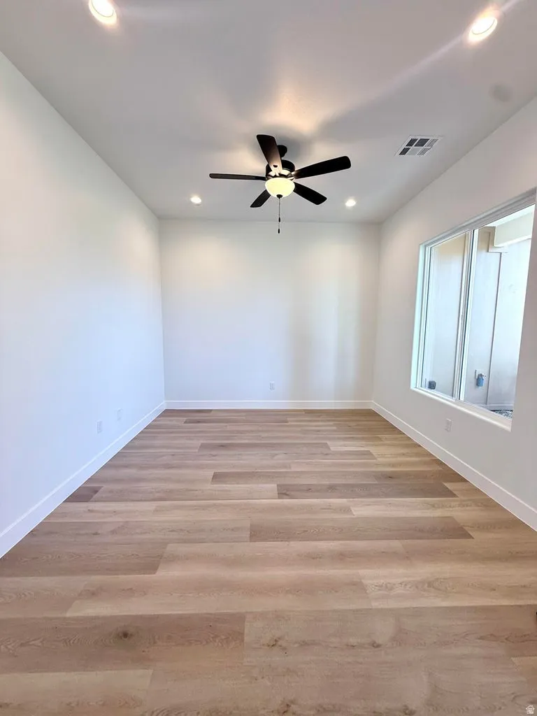 Spacious room featuring wood-finish flooring, white baseboards, and a ceiling fan with integrated lighting